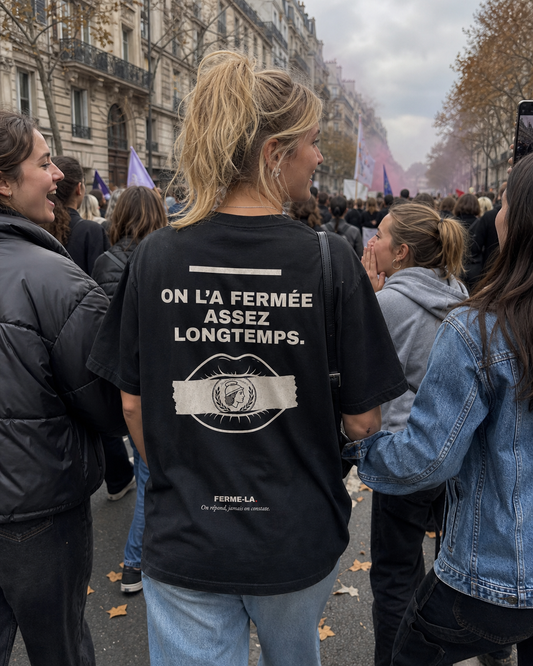 Une jeune femme porte le t-shirt de dos, au milieu d'une foule dans une rue de Paris.